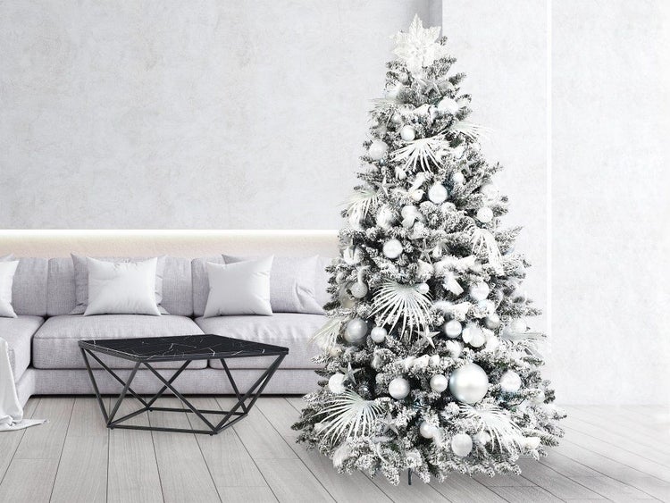 Geschmückter künstlicher Weihnachtsbaum mit Schneeoptik und Dekoration in einem modern eingerichteten Wohnzimmer mit Sofa und Couchtisch