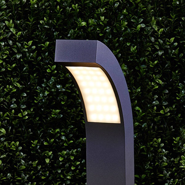 Moderne LED-Wegelampe in Anthrazit mit gebogener Form vor einer Hecke.