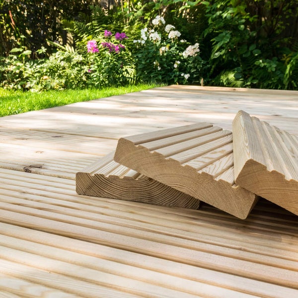 Terrassendielen aus Nadelholz mit geriffelter Oberfläche für den Gartenbau verlegt auf einer ebenen Fläche vor einem blühenden Garten.