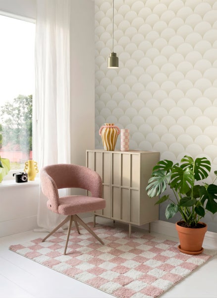 Modernes helles Zimmer mit Tapete im Schuppenmuster, rosa Polstersessel, kariertem Teppich, beigem Sideboard und einer Monstera-Pflanze.