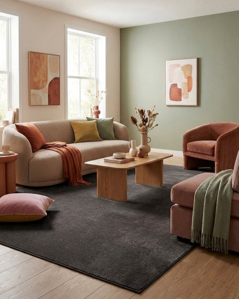 Modernes, helles Wohnzimmer mit dunkelgrauem Teppich, geschwungenem Sofa, Couchtisch aus Holz und Sesseln in Erdtönen auf Holzboden.