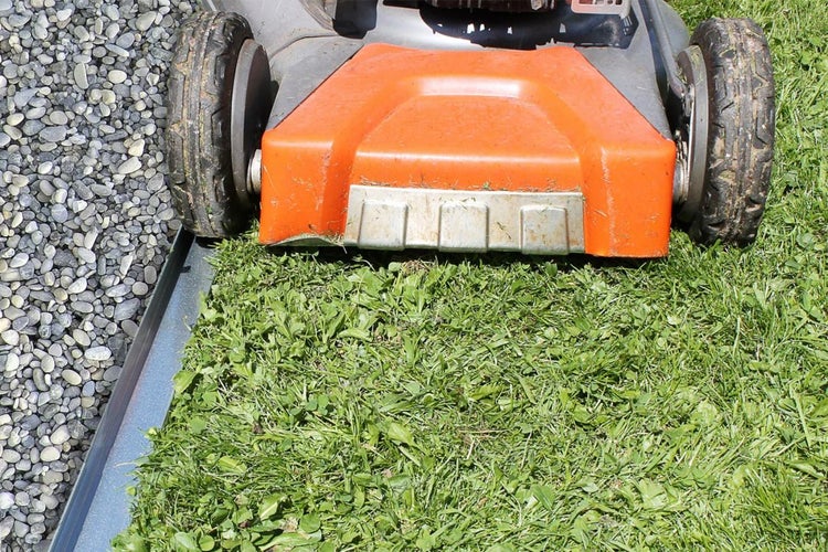 Rasenmäher beim Schneiden von Gras neben einer Kiesfläche.