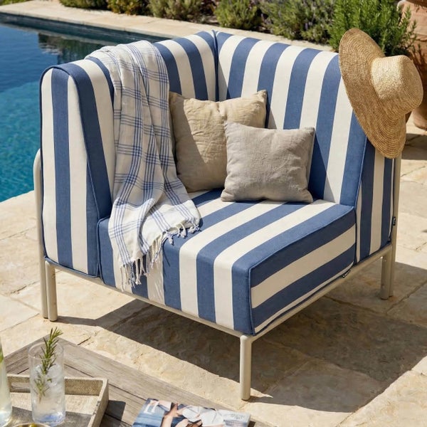 Moderner Garten-Lounge-Sessel mit blau-weiß gestreiftem Stoffbezug, zwei Kissen und einer Decke auf einer Terrasse am Pool.