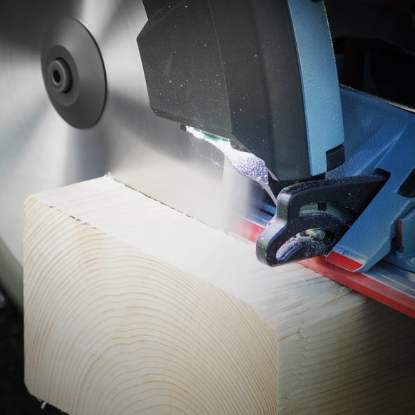 Nahaufnahme einer Kapp- und Gehrungssäge beim Schneiden eines massiven Holzbalkens mit integriertem LED Arbeitslicht.
