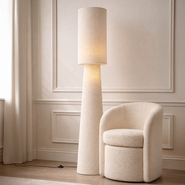 Moderne Stehleuchte mit Bouclé-Schirm und Fuß neben einem passenden Sessel in einem hellen, minimalistischen Raum mit Wandleisten.
