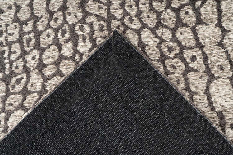 Teppich mit organischem Punktmuster und umgeschlagener Ecke, die die dunkle, strukturierte Rückseite zeigt.