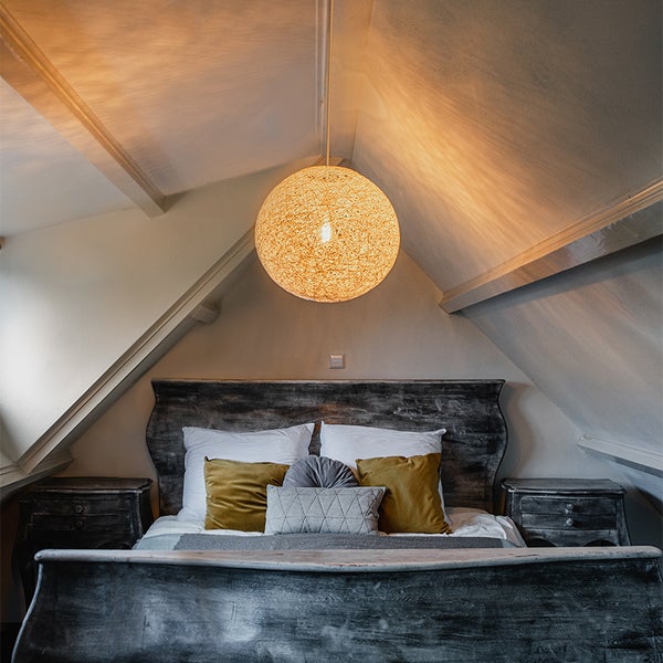 Dachschlafzimmer mit rustikalem Holzbett und einer großen, runden Pendelleuchte aus Geflecht unter der Dachschräge.