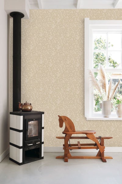 Wohnraum mit geblümter Tapete, einem schwarz-weißen Kaminofen, einem hölzernen Schaukelpferd und einem Fenster mit Trockenblumen.