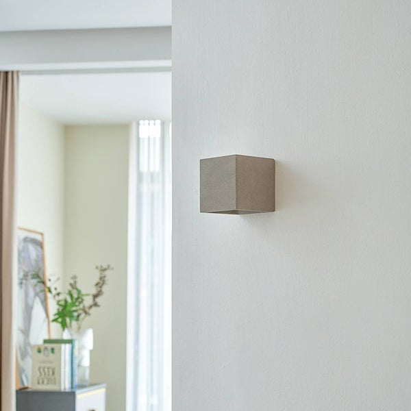 Moderne Wandleuchte in Würfelform mit Betonoberfläche in einem hellen, modern eingerichteten Innenraum.