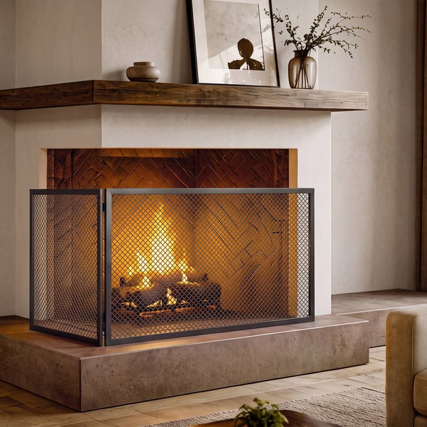 Ein dreiteiliges Metall-Kaminschutzgitter steht vor einem brennenden Kamin in einem gemütlichen Wohnzimmer mit Holzkaminumrandung.