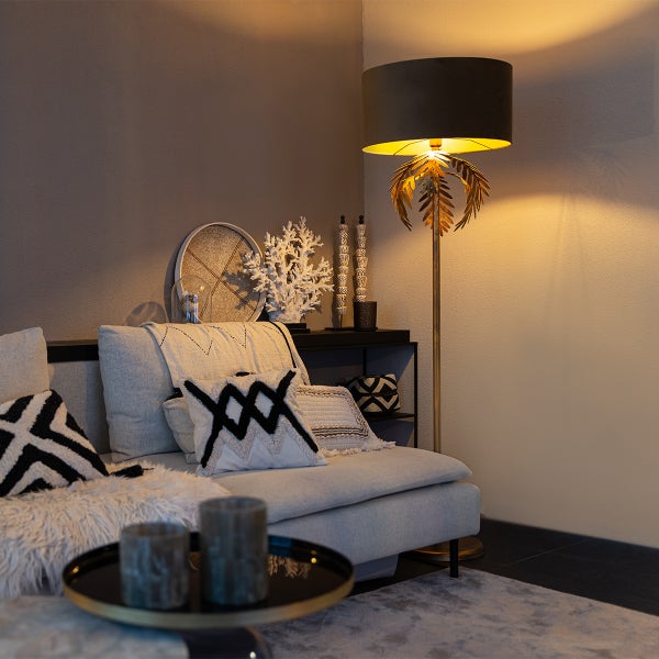 Wohnzimmer mit Sofa, Kissen, Beistelltisch und Stehlampe im goldenen Palmen Design.