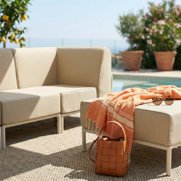 Moderne Gartenlounge mit beigefarbenem Sofa und Hocker auf einem Outdoorteppich am Pool.