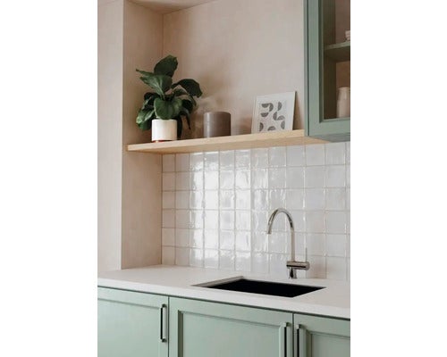 Moderne Küche mit weißen Wandfliesen, Chrom-Armatur, schwarzer Spüle, grünen Schränken und Holzregal mit Zimmerpflanze.
