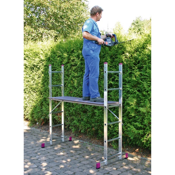 Mann auf einem Gerüst, der eine Hecke mit einer Heckenschere schneidet