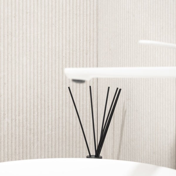 Moderne Armatur mit Duftstäbchen vor einer strukturierten Wandverkleidung im Badezimmer.