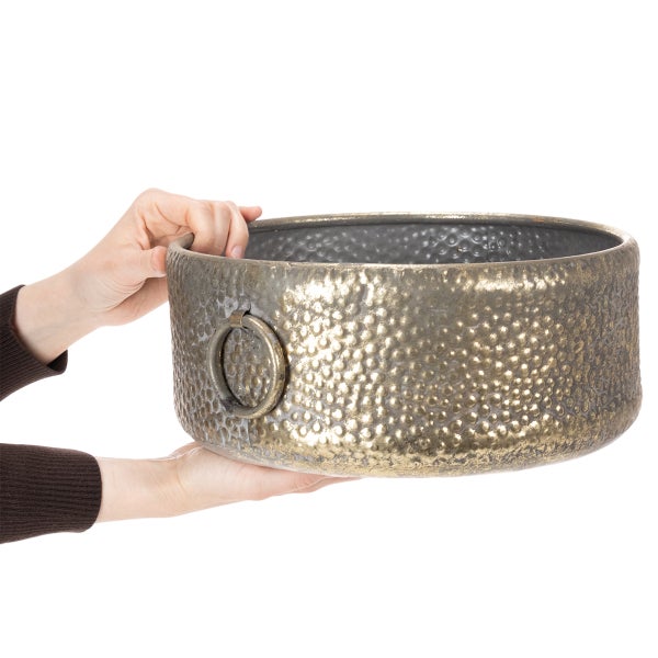 Goldfarbene Schale aus Metall mit gehämmerter Oberfläche und Ringgriff, in den Händen gehalten.