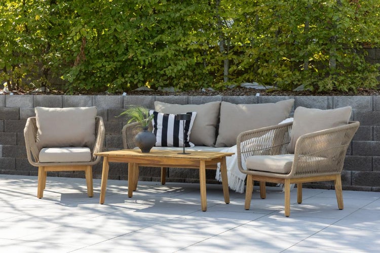 Gartenmöbel-Set aus einem Sofa, zwei Sesseln und einem Couchtisch aus Holz auf einer Terrasse vor einer Hecke und einer Steinmauer.