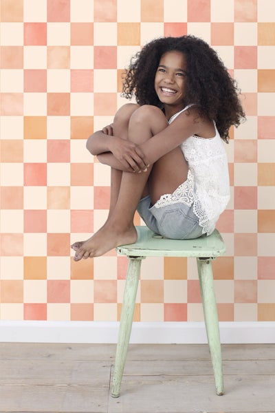 Mädchen sitzt auf einem Hocker vor einer Wand mit Schachbrettmuster.