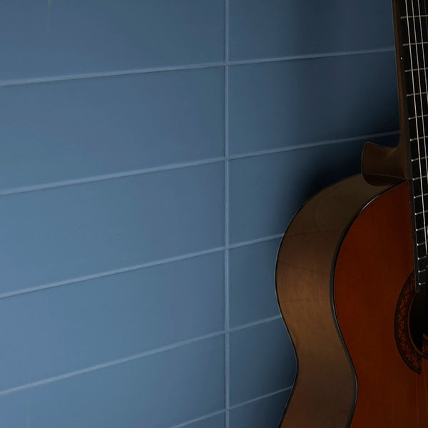 Rechteckige Wandfliesen in horizontaler Verlegung als Hintergrund einer akustischen Gitarre in einem Wohnraum.