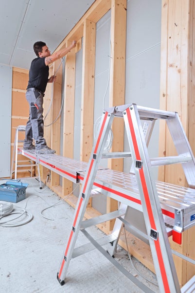 Handwerker auf einer Aluminium Arbeitsbühne von Hymer bei Installationsarbeiten im Innenausbau.