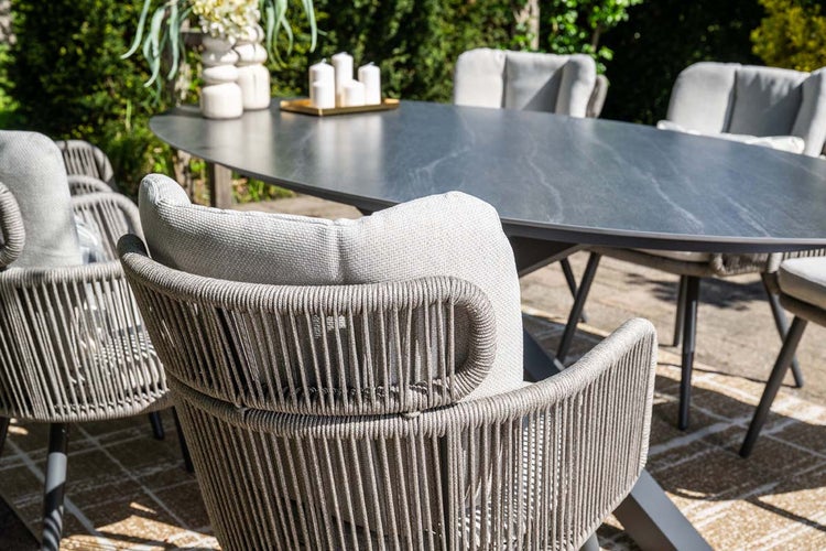 Moderner Gartentisch mit ovaler Platte in Steinoptik und Gartenstühlen aus grauem Seilgeflecht auf einer Terrasse.