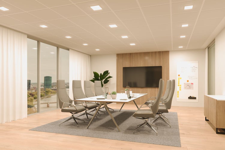 Moderner Konferenzraum mit weißem Besprechungstisch, grauen Bürostühlen, einer Holzlamellenwand mit TV, Stadtblick und heller Deckenbeleuchtung.