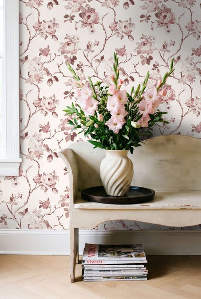 Wohnraum mit floraler Vliestapete, Vintage Sitzbank und einer Blumenvase vor einer Wand mit Rosenmotiv.