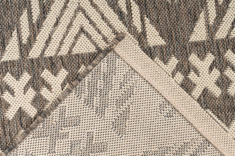 Detailaufnahme eines grau-beige gemusterten Flachgewebe-Teppichs mit geometrischem Design, umgeklappte Ecke zeigt Rückseite und Rand.