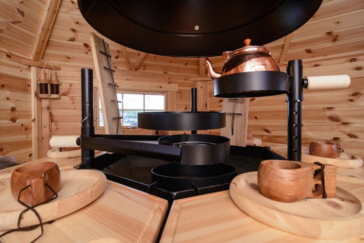 Innenansicht einer Grillkota mit Grill, Kupferkessel und Holztassen.