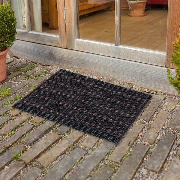 Eine rechteckige, gemusterte Fußmatte vor einer Terrassentür auf einem gepflasterten Außenbereich.