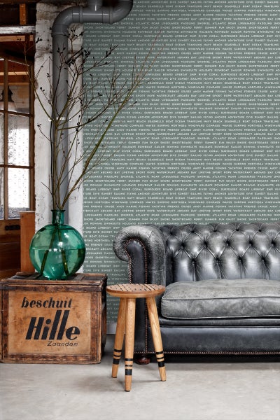 Dekoratives Wohnambiente mit Vintage-Ledersofa, Holzhocker, Holzkiste und grüner Glasvase