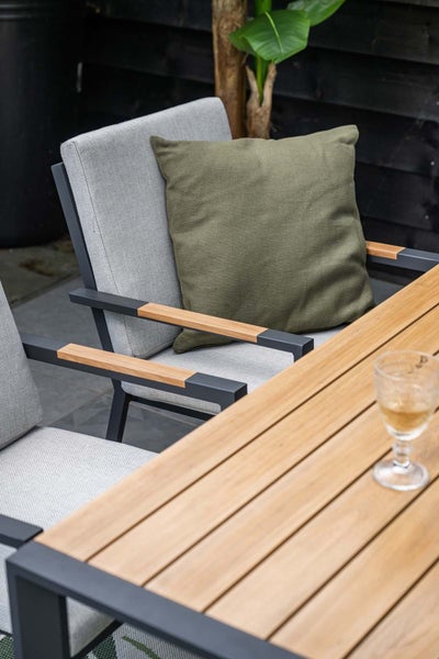 Modernes Gartenmöbel-Set bestehend aus Stühlen mit Stoffpolstern und Armlehnen aus Holz sowie einem Tisch mit Holzlatten auf einer Terrasse.