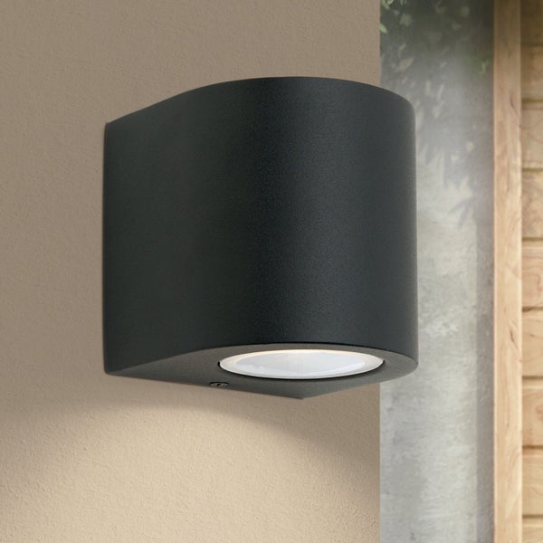 Moderne schwarze Außenwandleuchte in zylindrischer Form mit Lichtaustritt nach unten, an einer Wand montiert.