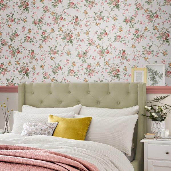 Schlafzimmer mit geblümter Tapete und gepolstertem Bett mit Knopfheftung, ergänzt durch strukturierte Bettwäsche und dekorative Wohnaccessoires.