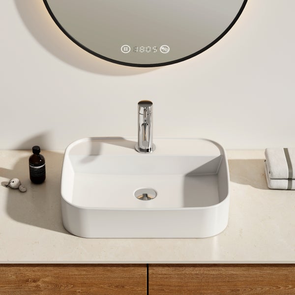 Modernes Badezimmer mit weißem, rechteckigem Aufsatzwaschbecken, verchromter Armatur und rundem Spiegel mit schwarzem Rahmen und Digitalanzeige.