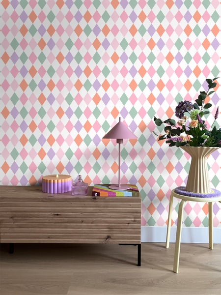 Wohnraum mit Rautenmuster-Tapete, Kommode, Tischleuchte und Blumenarrangement.