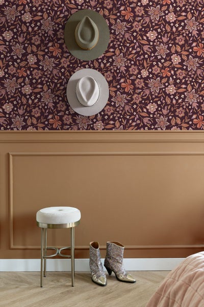 Vliestapete mit floralem Muster in Rosa und Orange auf dunklem Grund, kombiniert mit brauner Wandvertäfelung und einem Hocker.