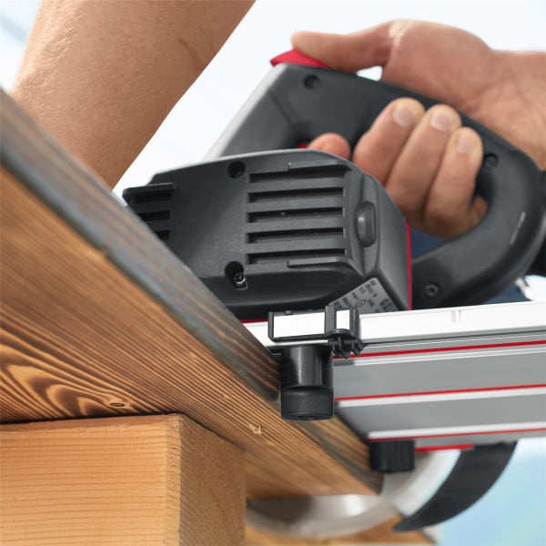 Hand eines Arbeiters führt eine elektrische Handkreissäge mit Führungsschiene beim Zuschneiden eines Holzbretts.