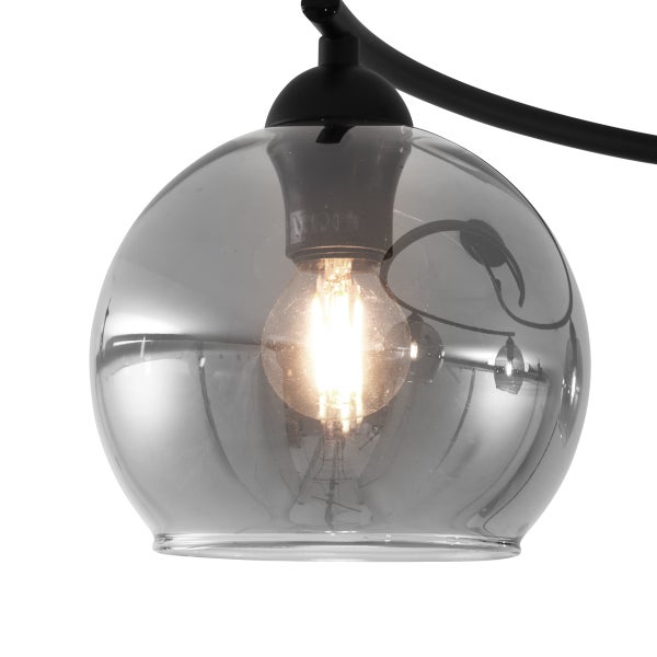 Nahaufnahme einer Pendelleuchte mit rauchiger Glaskugel und leuchtender Glühbirne an einer schwarzen Metallhalterung.