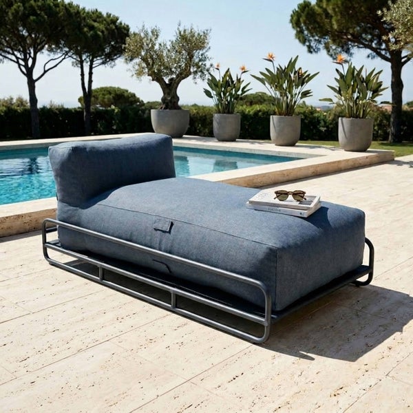 Moderne Gartenliege mit blauem Polster auf dunklem Metallgestell, platziert auf einer hellen Steinterrasse neben einem Pool im Freien.