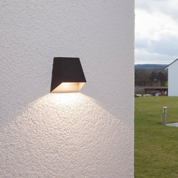 Moderne LED Außenwandleuchte in Keilform an einer weißen Fassade, warmweißes Licht strahlt nach unten ab.