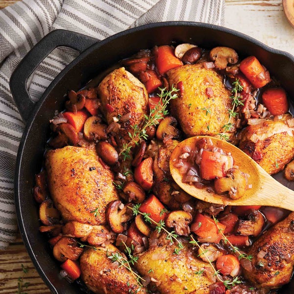 Gebratenes Hähnchen mit Gemüse in einer gusseisernen Pfanne mit Holzlöffel.
