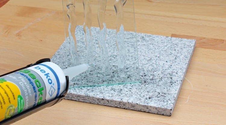 Anwendung von transparentem beko Gecko Kleb- und Dichtstoff auf einer Glasscheibe zur Verklebung mit einer Granitplatte.
