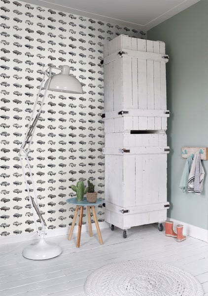 Einrichtungsidee für ein Kinderzimmer mit Mustertapete, Stehlampe und Holzschrank auf Rollen.