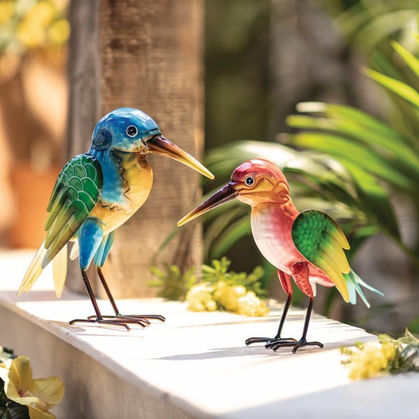 Zwei dekorative Gartenfiguren aus Metall in Form von Vögeln, ein blau-gelber und ein rot-gelber Vogel auf einer Mauer.
