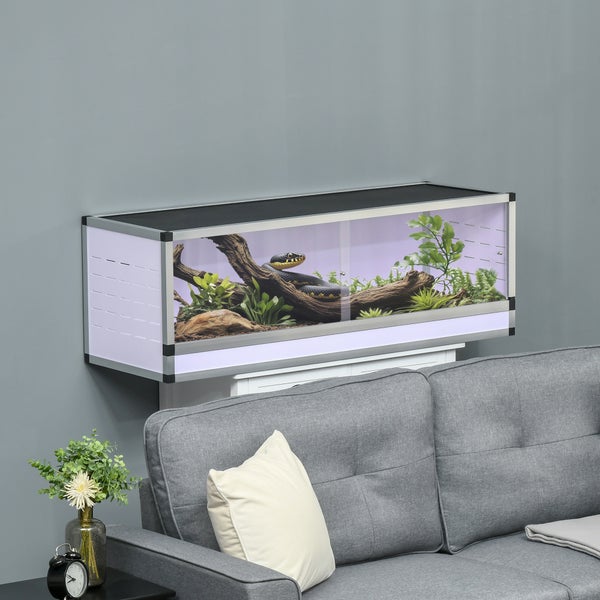 Rechteckiges Terrarium mit Aluminiumrahmen, einer Schlange auf Wurzelholz und Pflanzen, platziert in einem Wohnzimmer über einem Sofa.