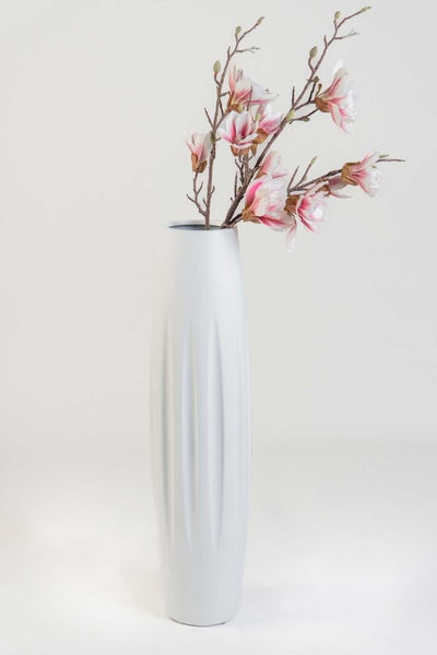 Hohe weiße Vase mit vertikalen Rillen und künstlichen Magnolienzweigen mit rosa-weißen Blüten.