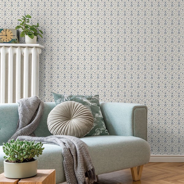 Wohnzimmer mit Sofa, Zimmerpflanzen und floral gemusterter Tapete.