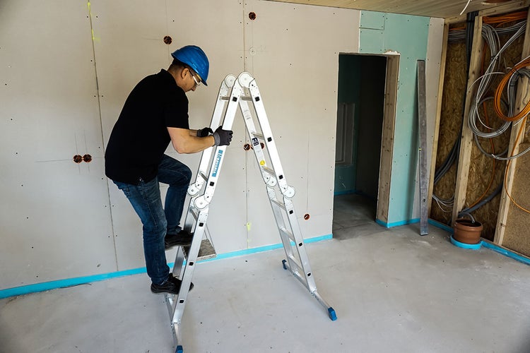 Handwerker auf Mehrzweckleiter bei Renovierungsarbeiten in Innenräumen