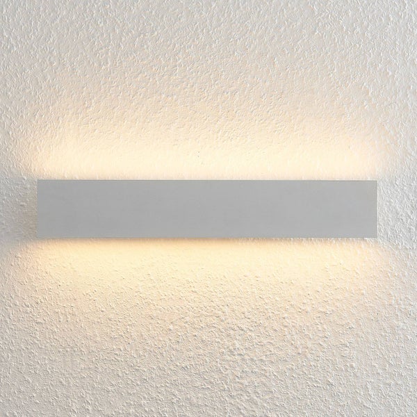 Moderne silberne rechteckige Wandleuchte aus Metall mit warmem Lichtaustritt nach oben und unten auf einer strukturierten Oberfläche.